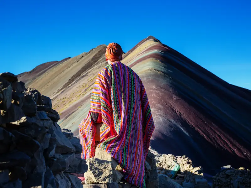Turista brasileiro com poncho colorido admirando a Montanha Colorida no tour de 8 dias em Cusco